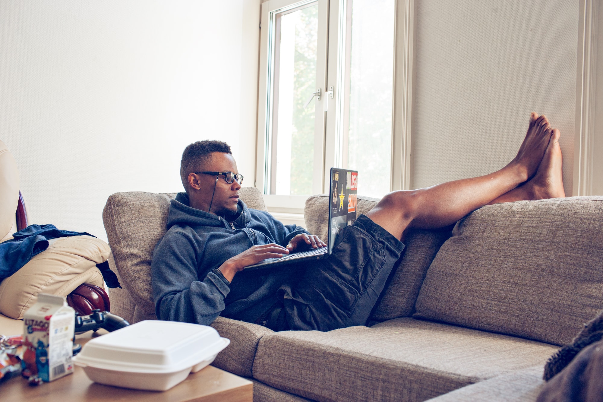 En mann arbeider med en laptop fra sofaen hjemme